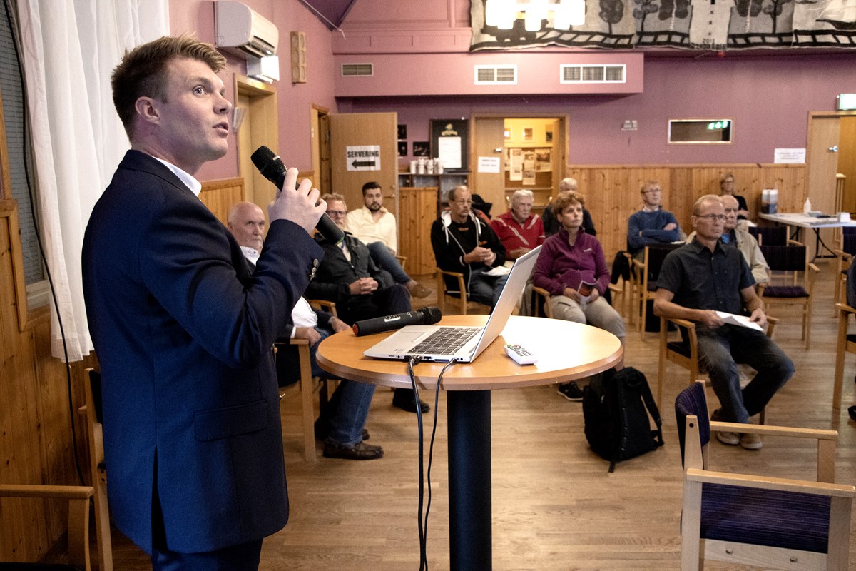 Max Bjurström står framför besökarna med en mikrofon i handen, framför munnen, som han pratar i.