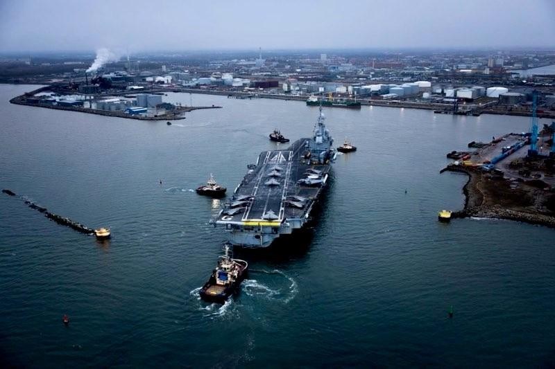 Drönarbild över hangarfartyg anlöper hamn.