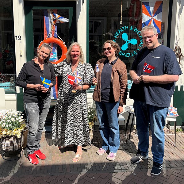 Fyra personer som håller i varsin flagga, framför entrén till den danska sjömansklubben i Brielle.