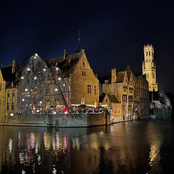 En vy i en stad i ARA-området. Vatten i förgrunden, gamla upplysta byggnader på andra sidan vattnet och ett torn i bakgrunden.