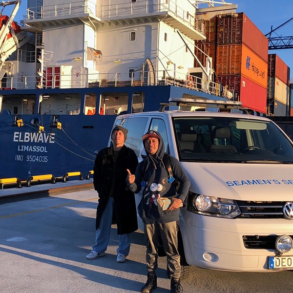 Two seafarers standing by the minibus parked in front of their ship