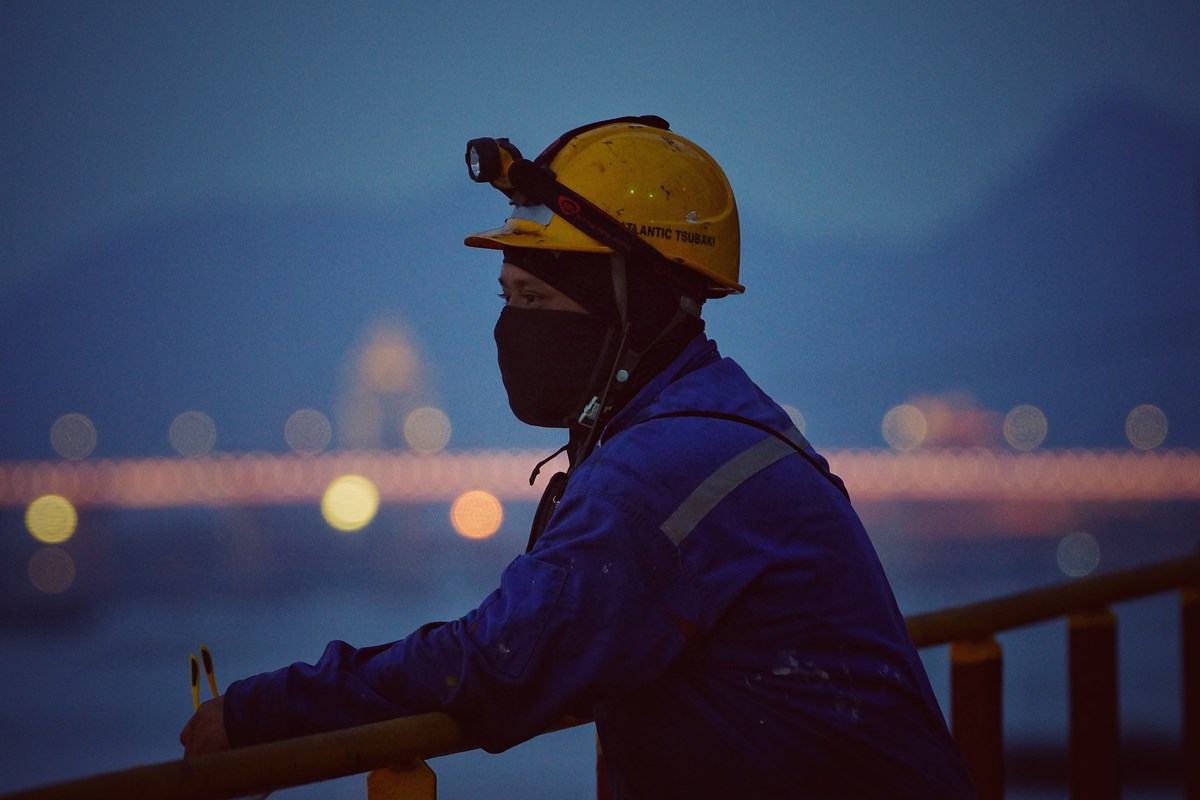 Seafarer with helmet standing by the ships rail and looking out
