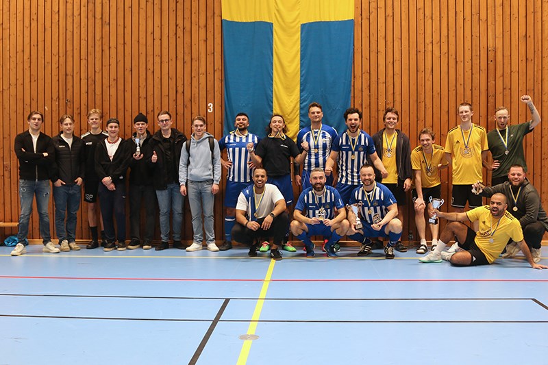 Samtliga vinnarlag (1-3) uppställda mot sporthallens vägg, hållandes sina respektive pokaler