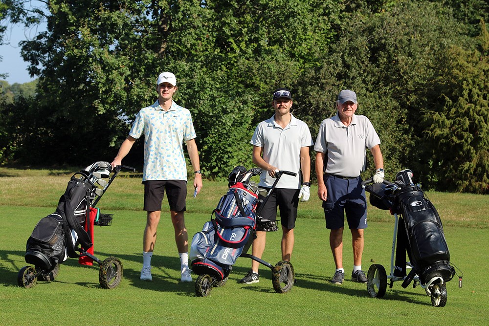 Tre golfspelare står uppställda med sina golfbagar och tittar in i kameran