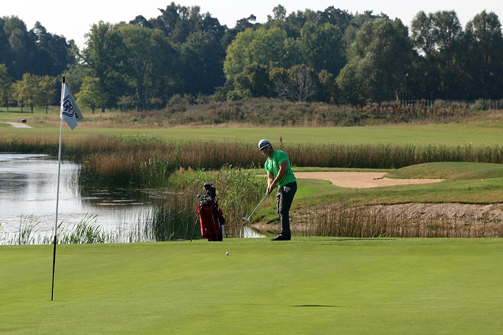 Ensam golfspelare puttar bollen mot hålflaggan, som står i hålet. Sandbunker och vattenhinder i bakgrunden